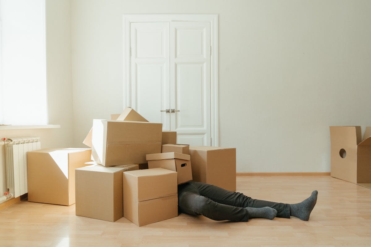 Déménagement : comment transformer cette épreuve en étape sereine Person on floor surrounded by cardboard boxes during moving; concept of stress and relocation.