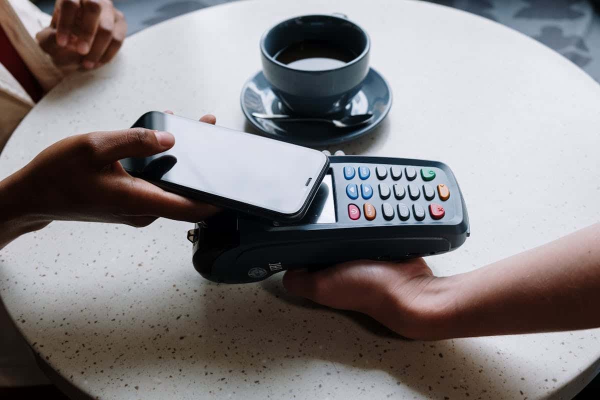 Anonyme, sécurisé, approuvé par Apple : les amateurs de tech adoptent le prépayé A person using a smartphone to make a contactless payment with a card reader on a cafe table.
